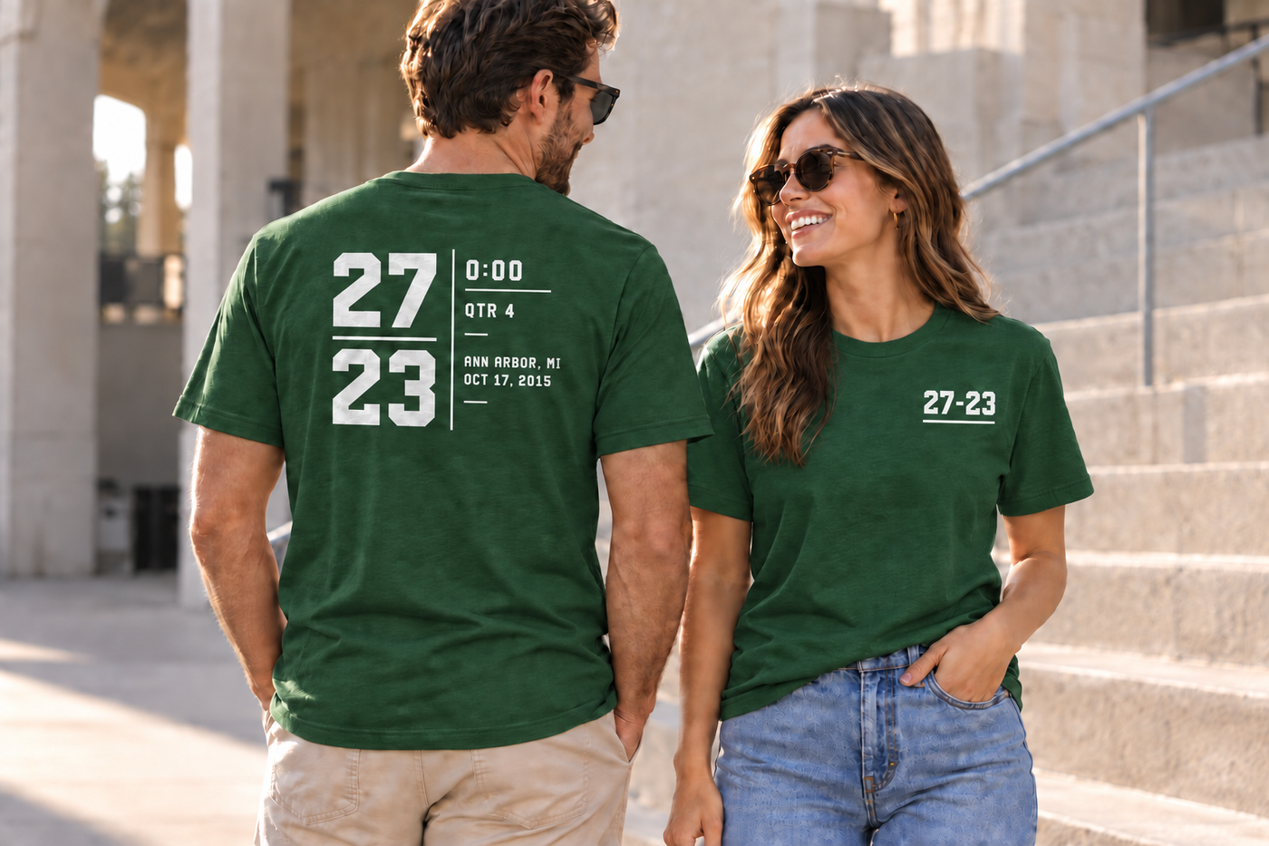Generated lifestyle preview showing two adults wearing the same Michigan State 27–23 Classic shirt, with its front and back designs visible.